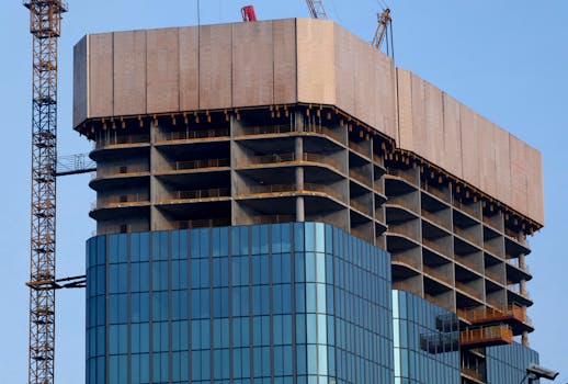 High-rise building under construction with cranes and glass facade in daylight.