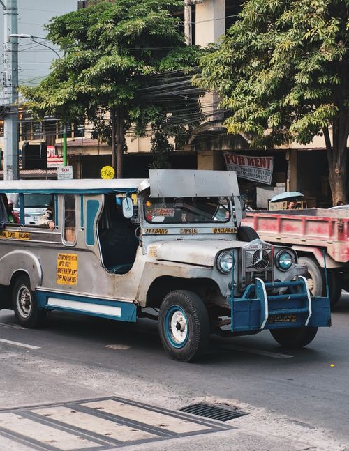 Free A classic jeepney carrying passengers rides through a bustling street in Manila, offering local public transport. Stock Photo