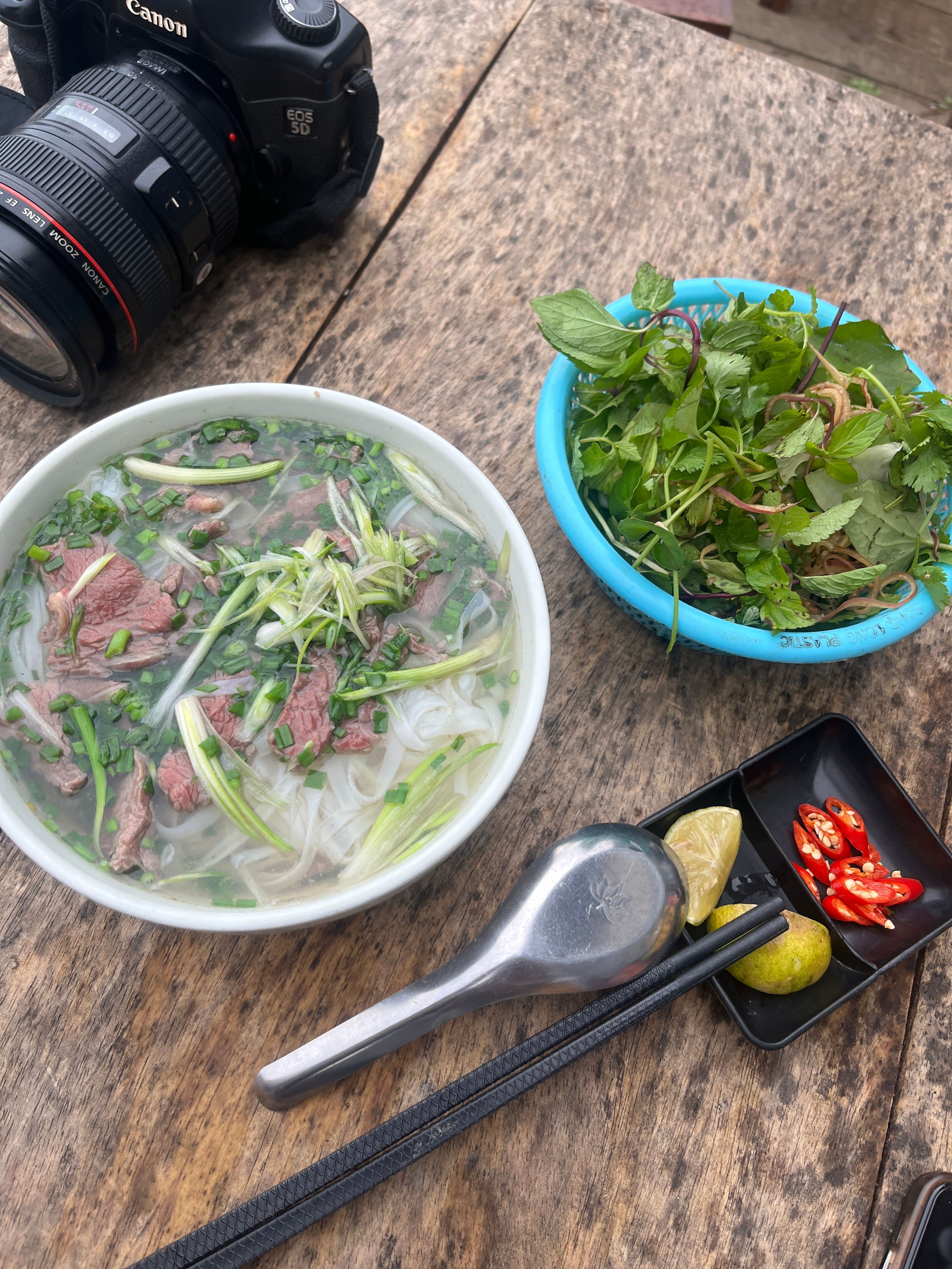 A steaming bowl of Vietnamese pho with fresh herbs and chili on a rustic wooden table, perfect for food enthusiasts.