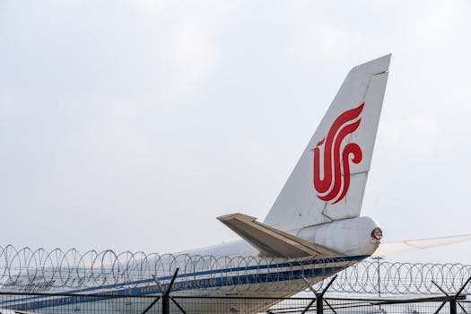 Airplane tail with red logo behind barbed wire, under clear sky.