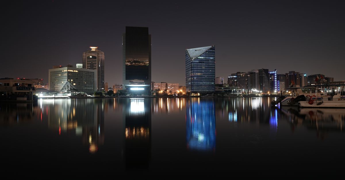 Capture of Dubai skyline at night with reflections in water, showcasing modern architecture.
