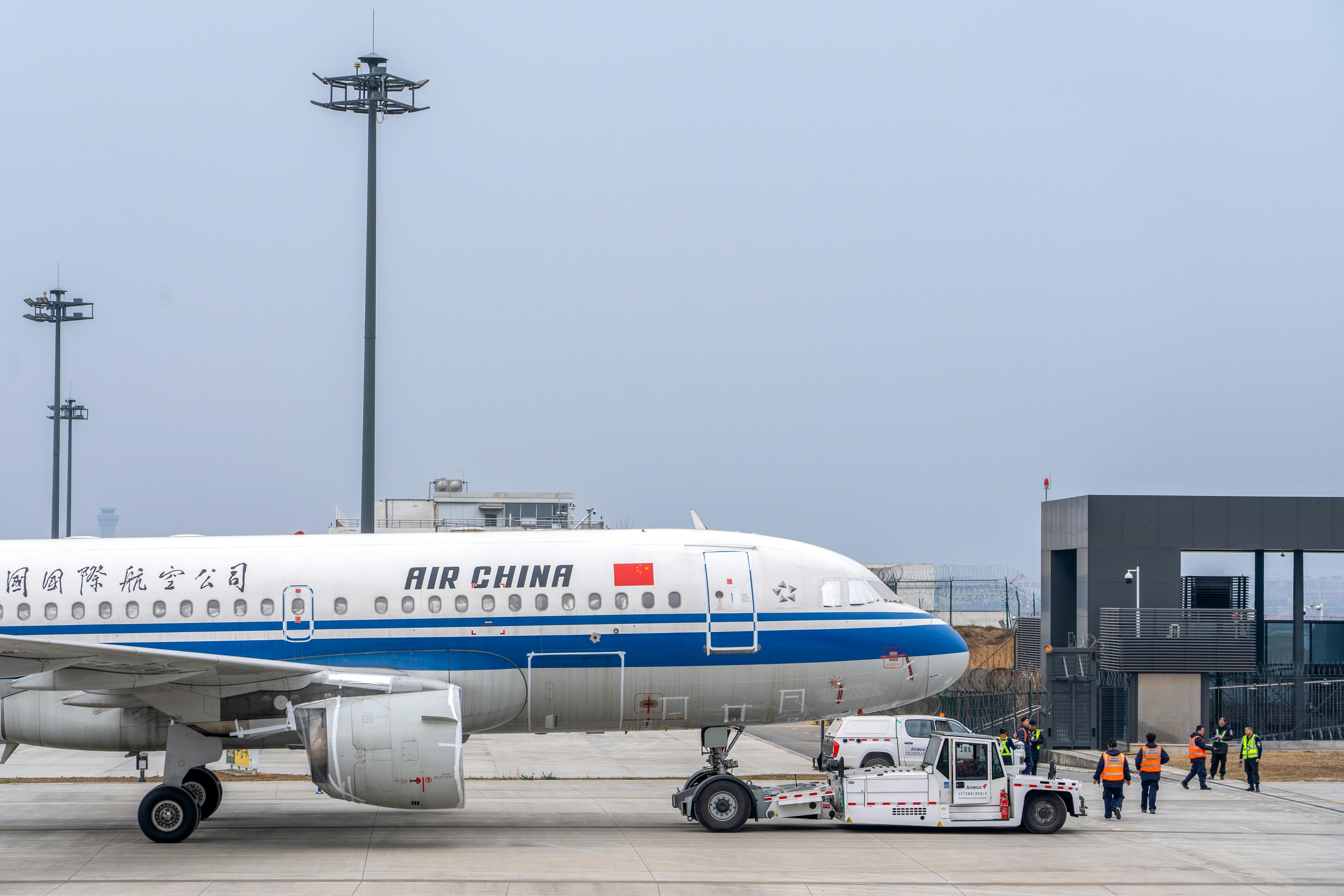 Air China airplane being maneuvered on the runway by ground staff at an airport.