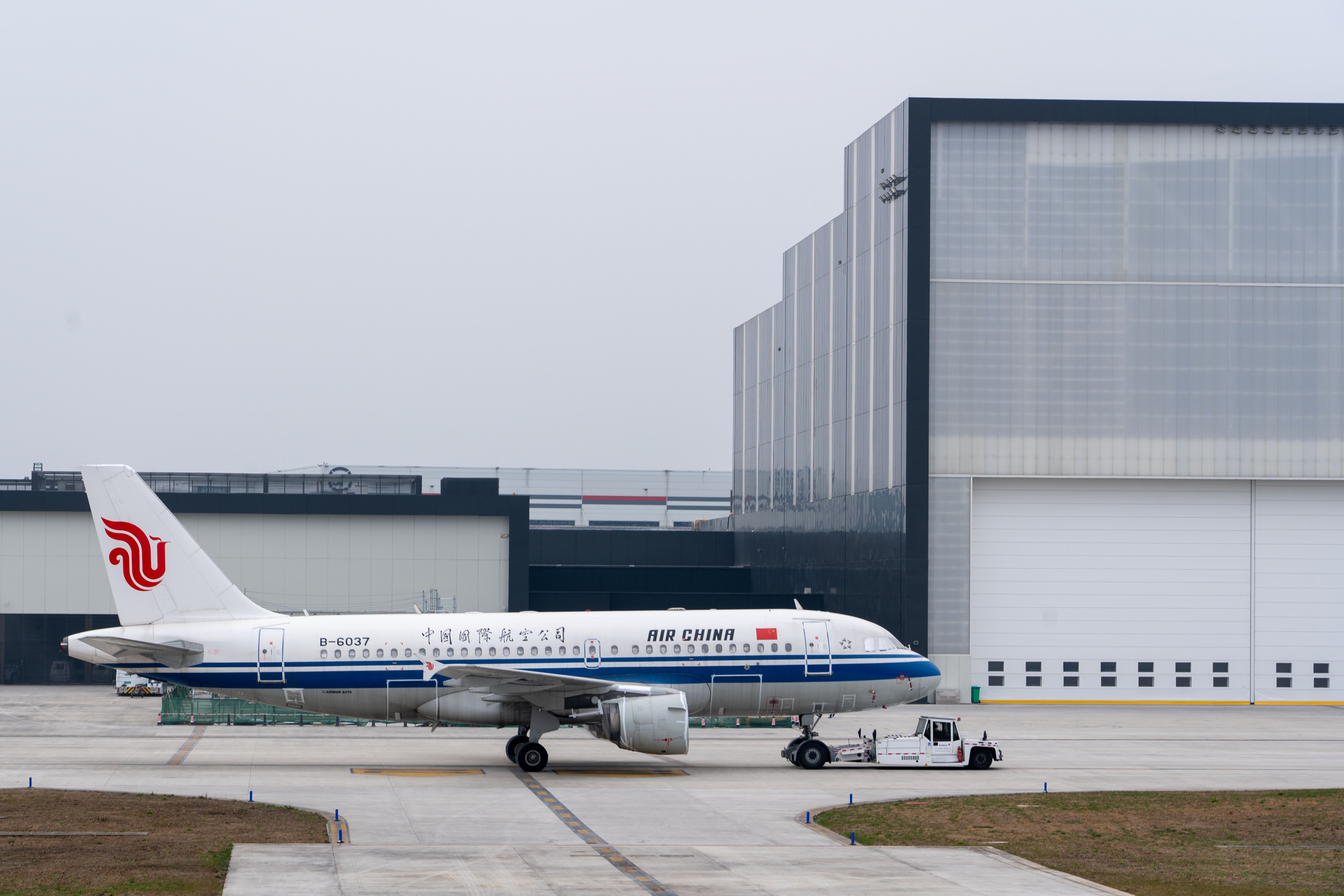 Air China plane parked at an airport hangar on a cloudy day, ready for takeoff.