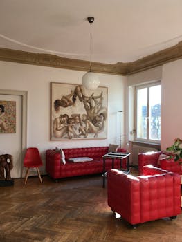 Stylish lounge showcasing red furniture, artwork, and natural light through large windows.