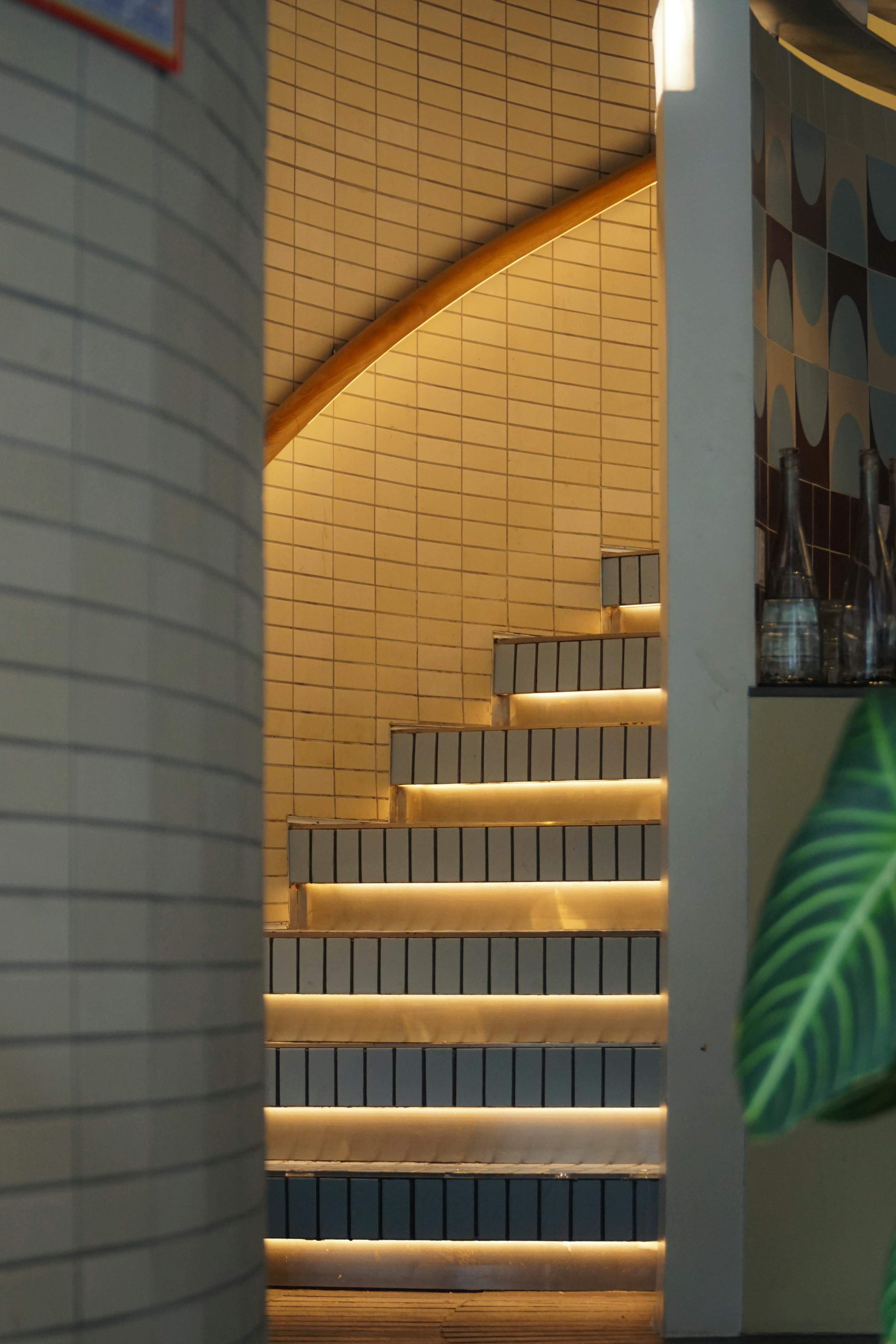 Free Elegant curved staircase with ambient lighting and tiled walls in a contemporary setting. Stock Photo