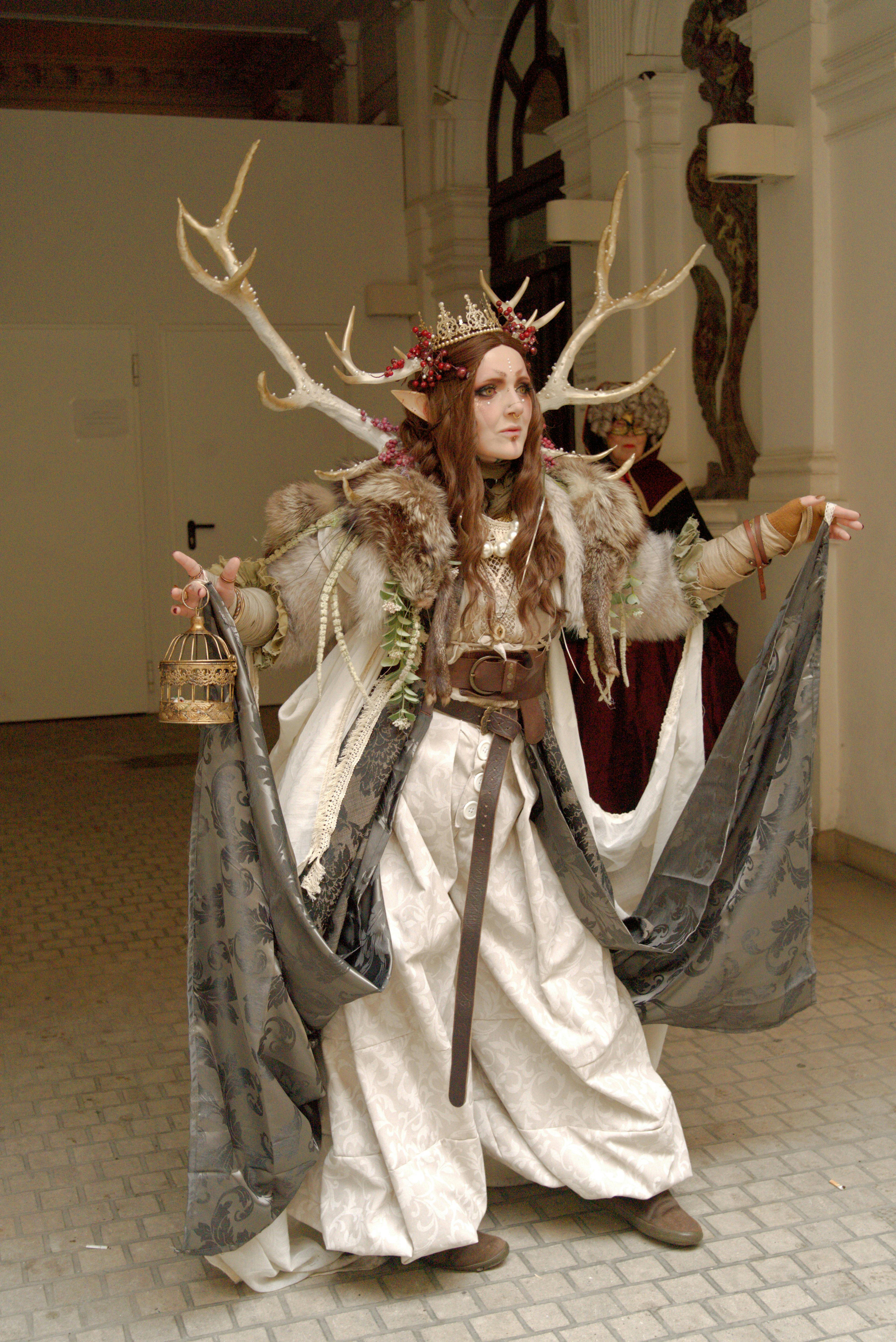 grátis Mulher vestida com uma elaborada fantasia e um adorno de cabeça com chifres, em pé dentro de casa. Foto profissional