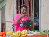 Young Tanzanian vendor arranging produce at market stall in vibrant setting.