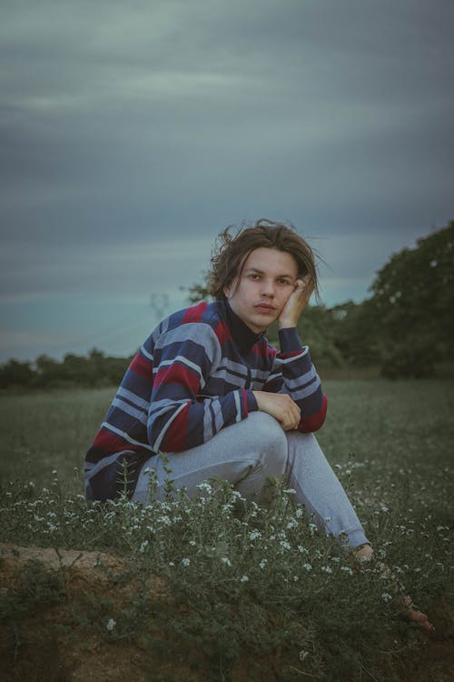 Young pensive male sitting in grassy meadow