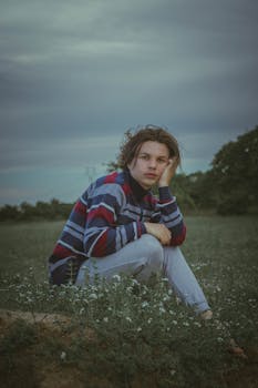 一个年轻人坐在阴云密布的草地上沉思，四周是大自然的景象