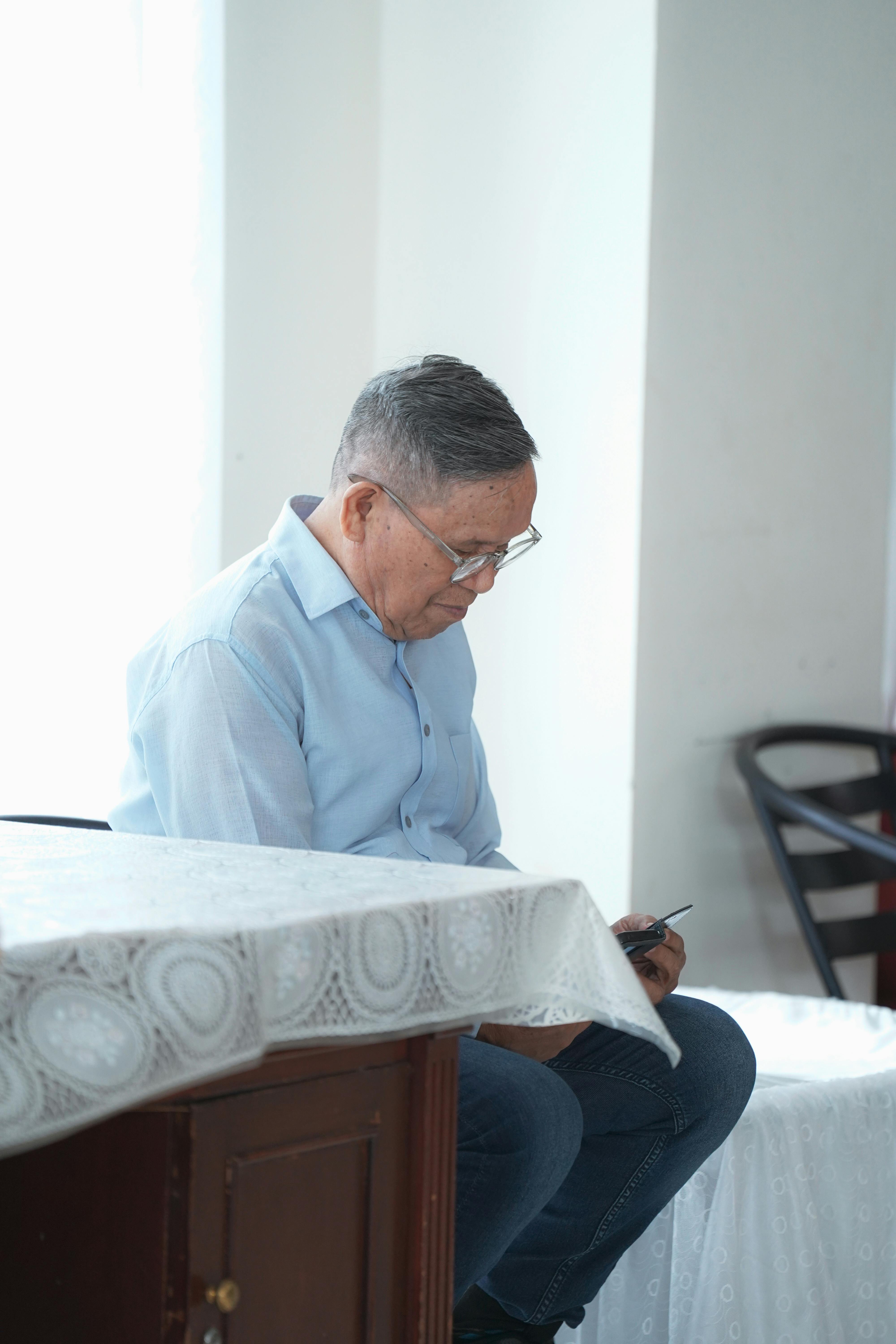 Kostnadsfria Äldre man läser på sin smartphone inomhus i Jakarta, Indonesien, klädd i vardagskläder. Stock foto