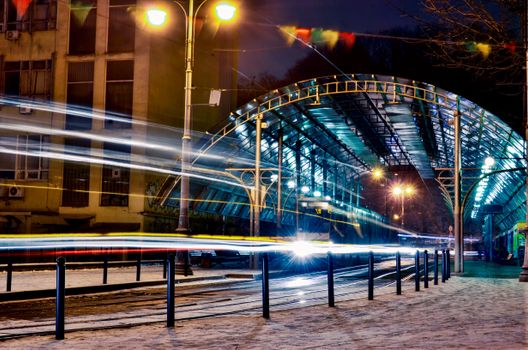 Vivid light trails at a tram station in Lviv, Ukraine captured at night in a dynamic urban scene.