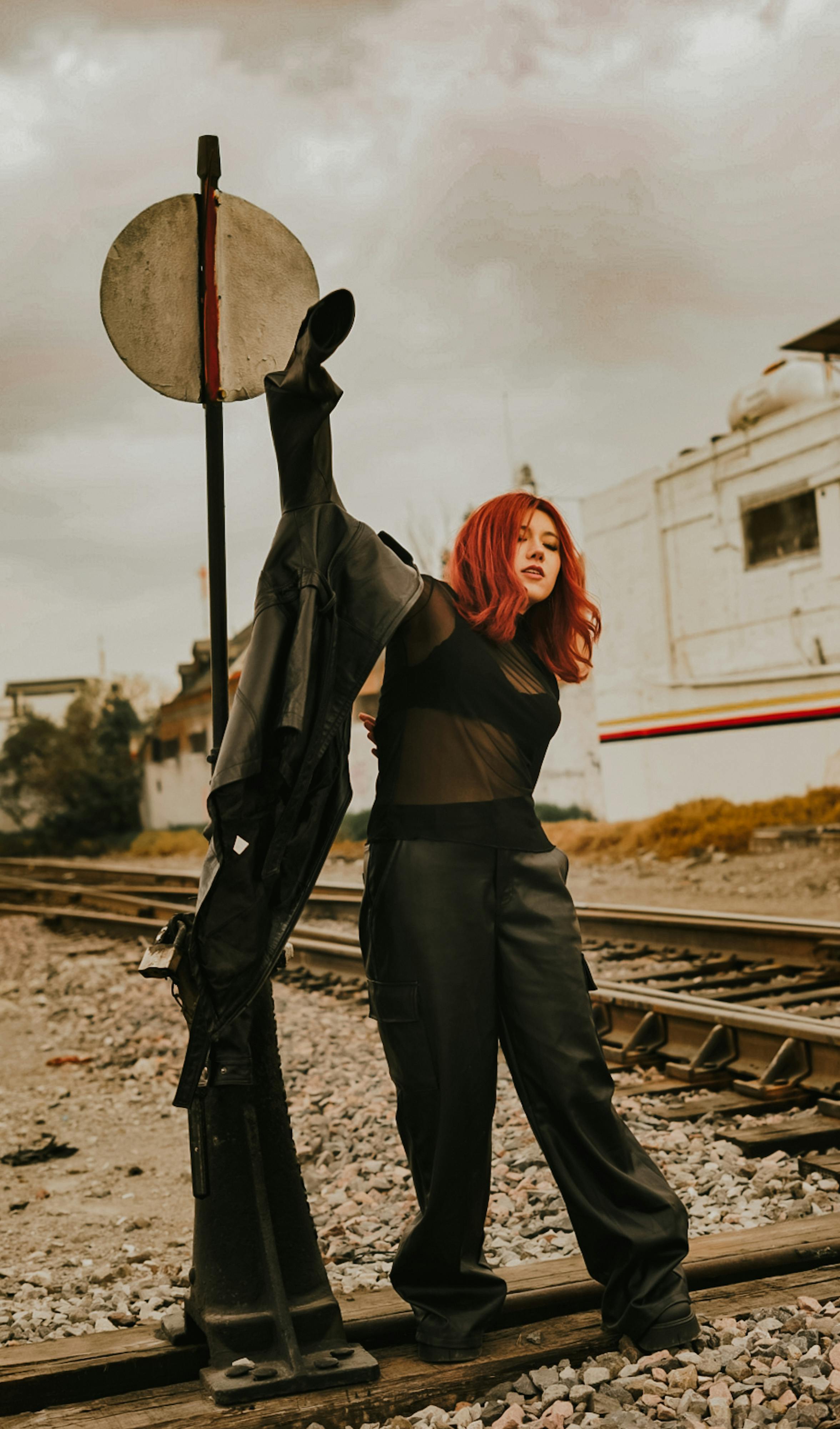 免费 一位红发时尚女子身着黑色服装，在铁轨旁摆出极具戏剧性的姿势。 素材图片