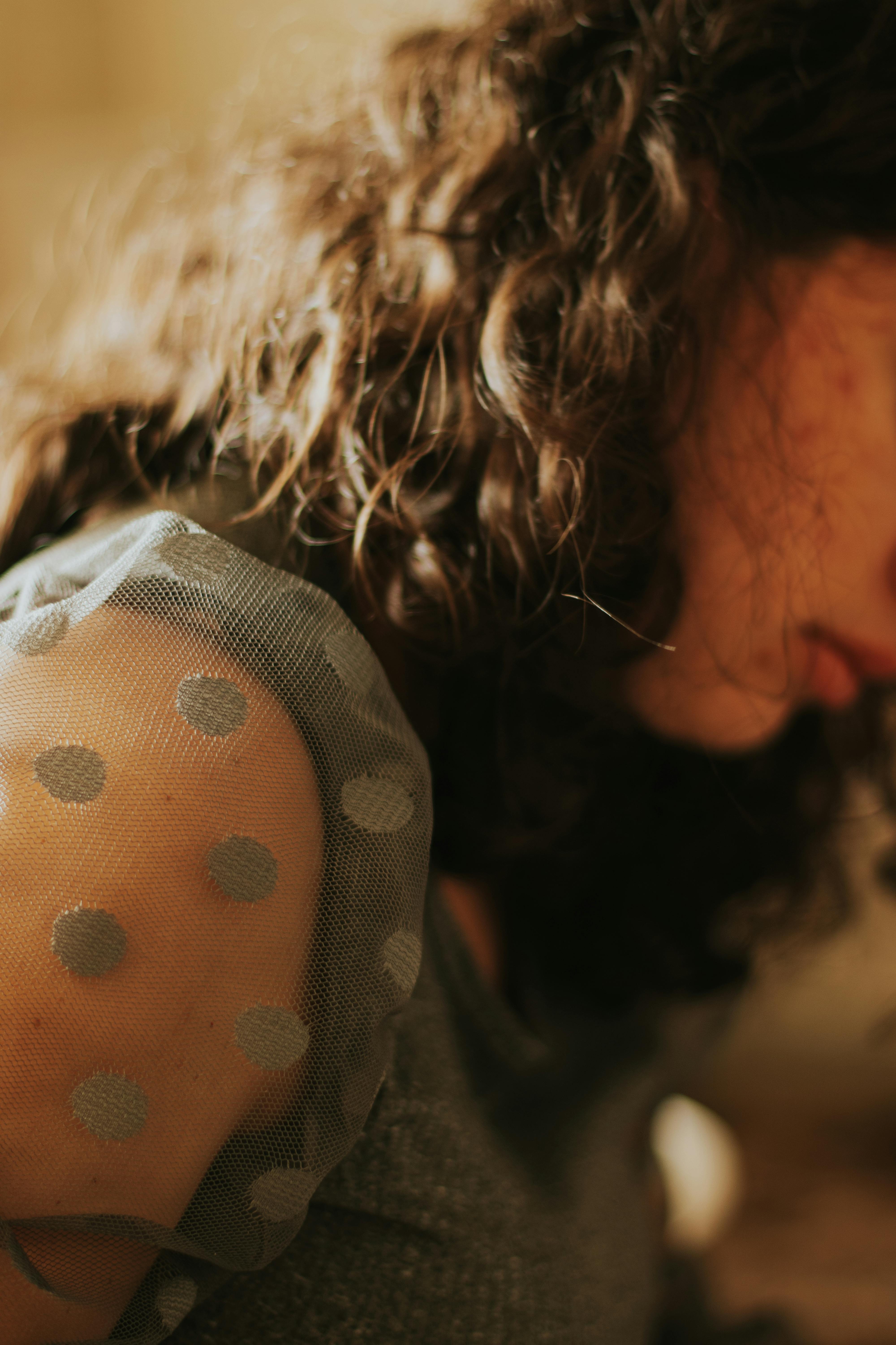 Ücretsiz Kadının kıvırcık saçlarına ve puantiyeli koluna odaklanan yumuşak çekim, sakin bir atmosfer yaratıyor. Stok Fotoğraflar