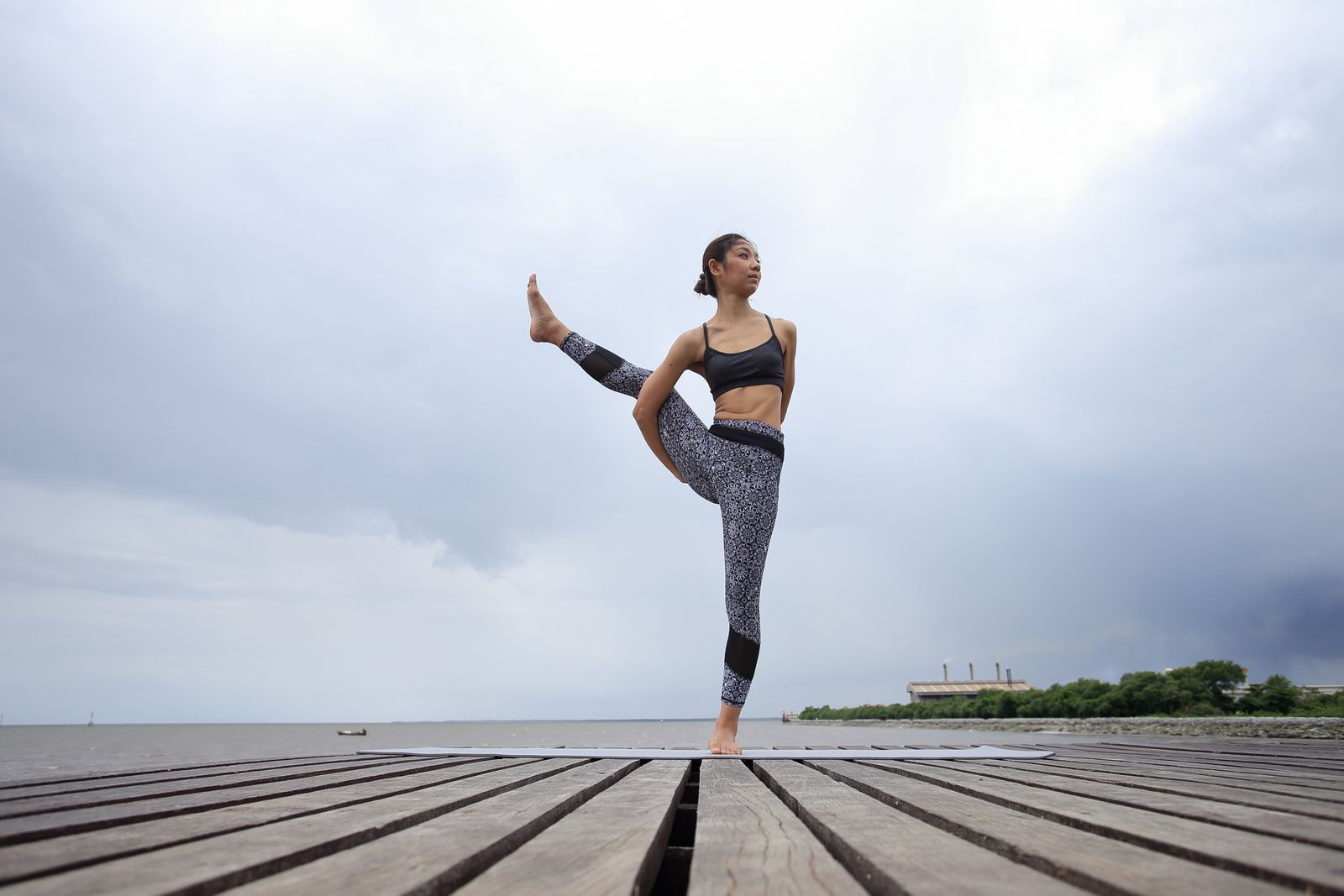 Woman balancing on one leg in an eka pada yoga pose on a wooden dock by the water