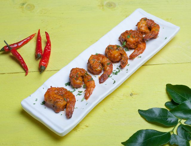 Delicious spicy grilled shrimp garnished with herbs and served with red chili peppers.