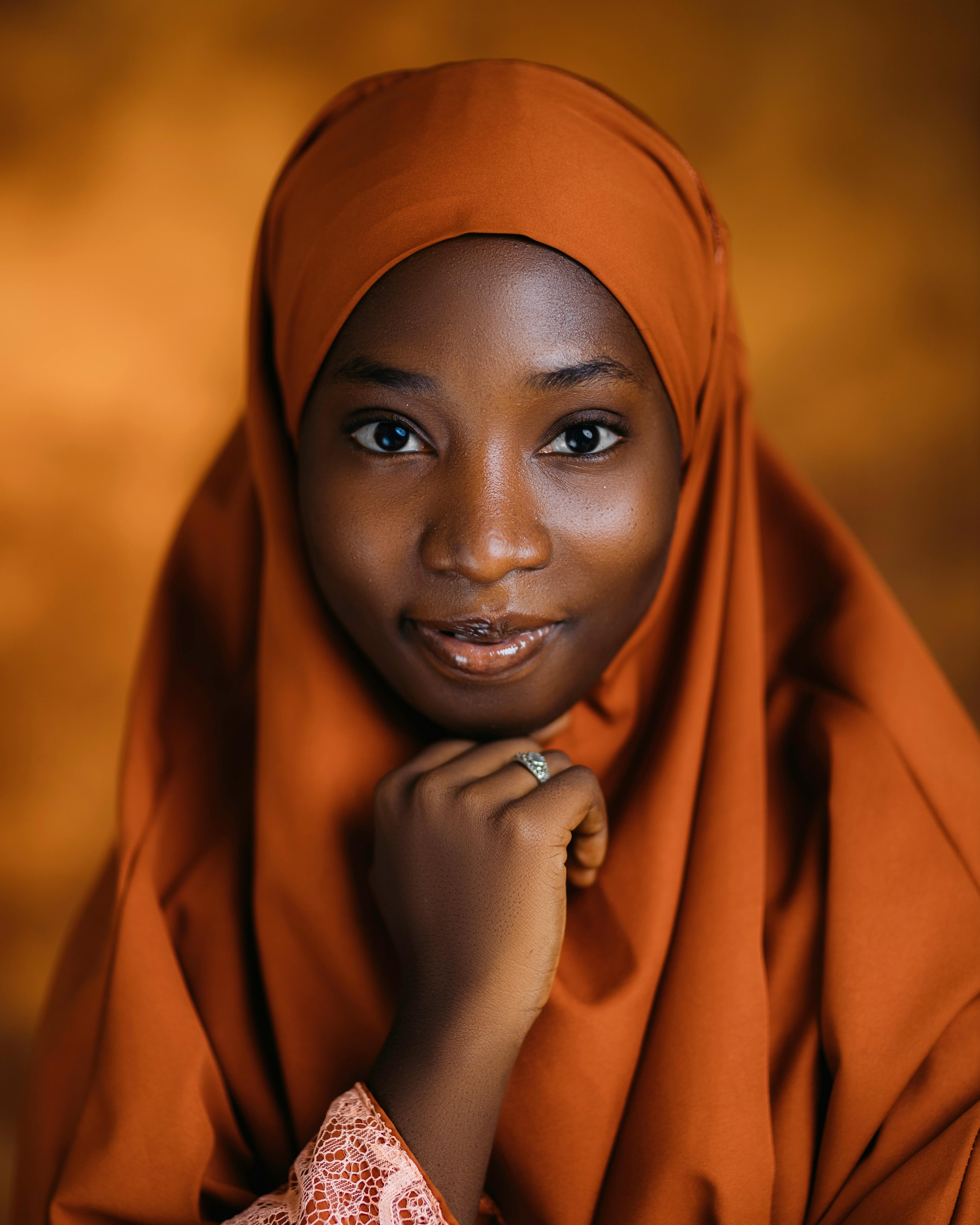 Charming portrait of a young woman in an orange hijab with a warm smile. Captures elegance and cultural beauty.