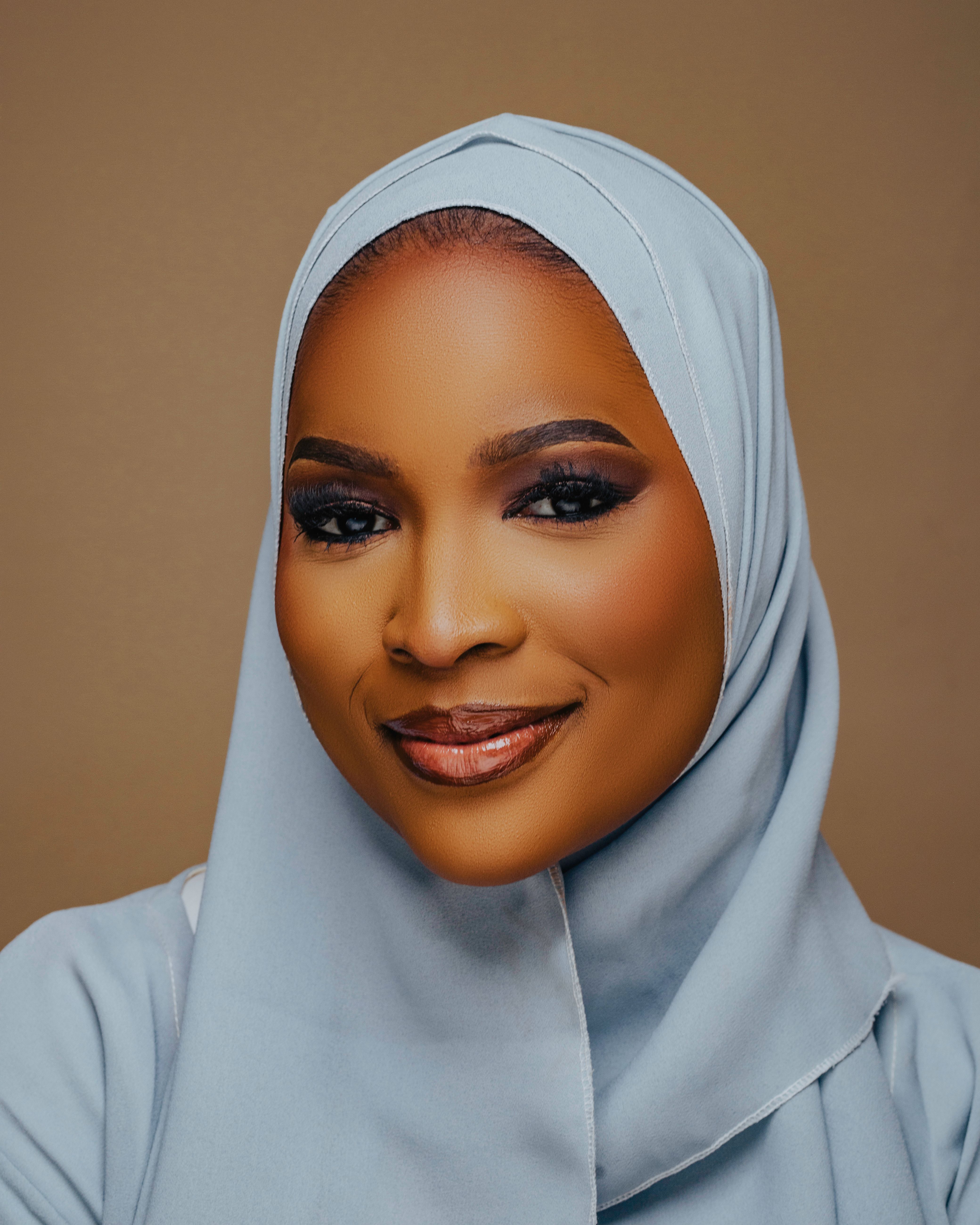 Close-up portrait of a confident woman wearing a light blue hijab, smiling warmly in a neutral background setting.