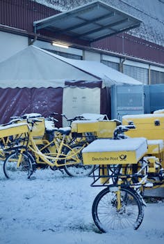 Yellow Deutsche Post bicycles covered in snow, parked outdoors in a cold winter scene.