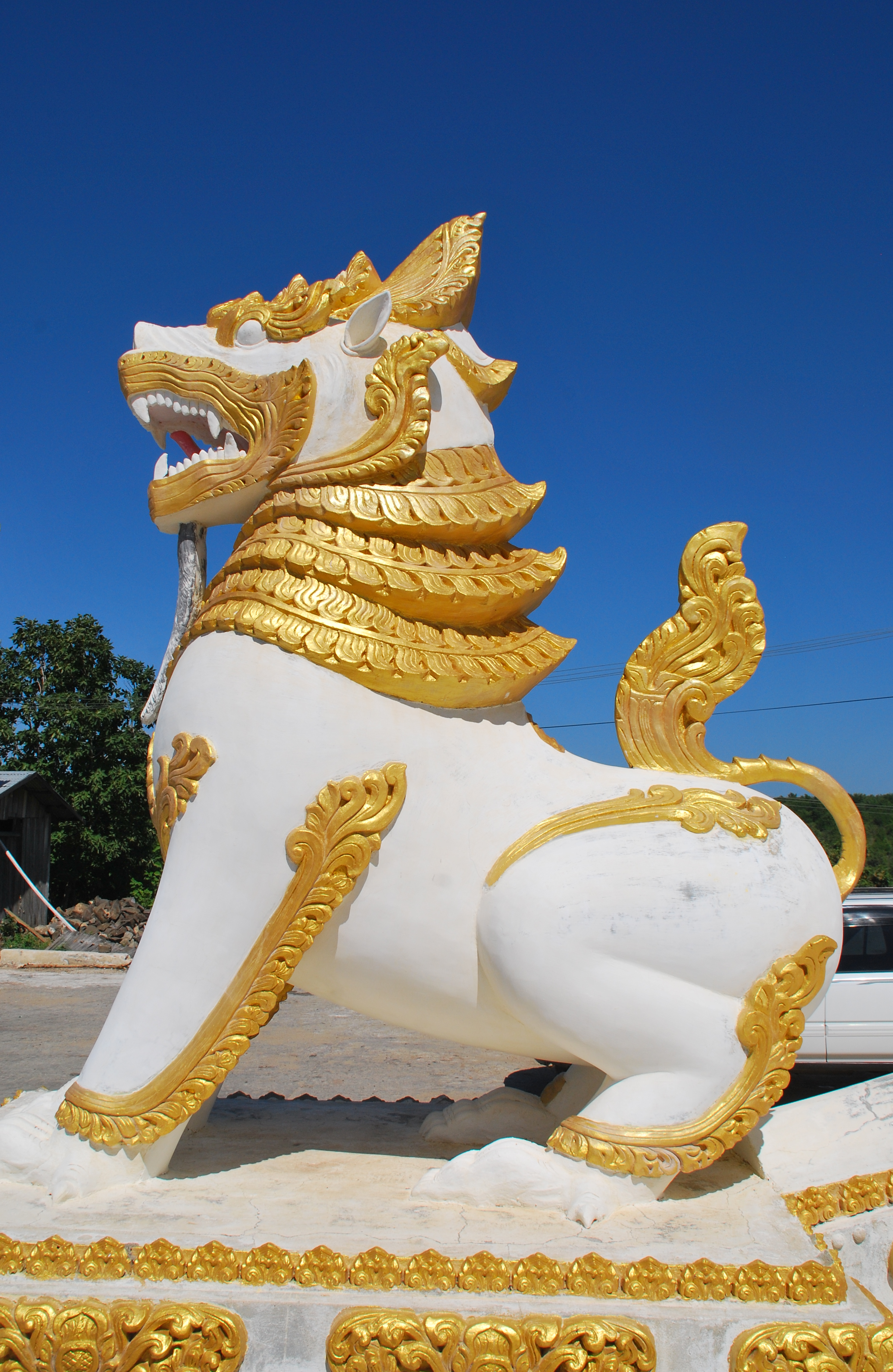 A majestic white and gold Singha statue under a clear blue sky, symbolizing strength.