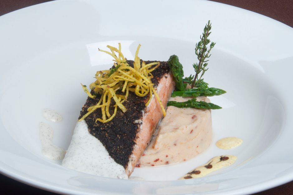 A charred, deep-red-black spiced redfish fillet in a cast iron skillet, with a lemon wedge and pat of melted butter on top.