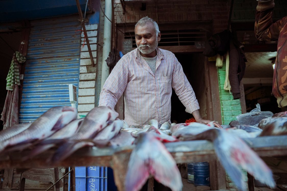 Free A fishmonger displays fresh fish at an outdoor market stall, showcasing a traditional local market scene. Stock Photo