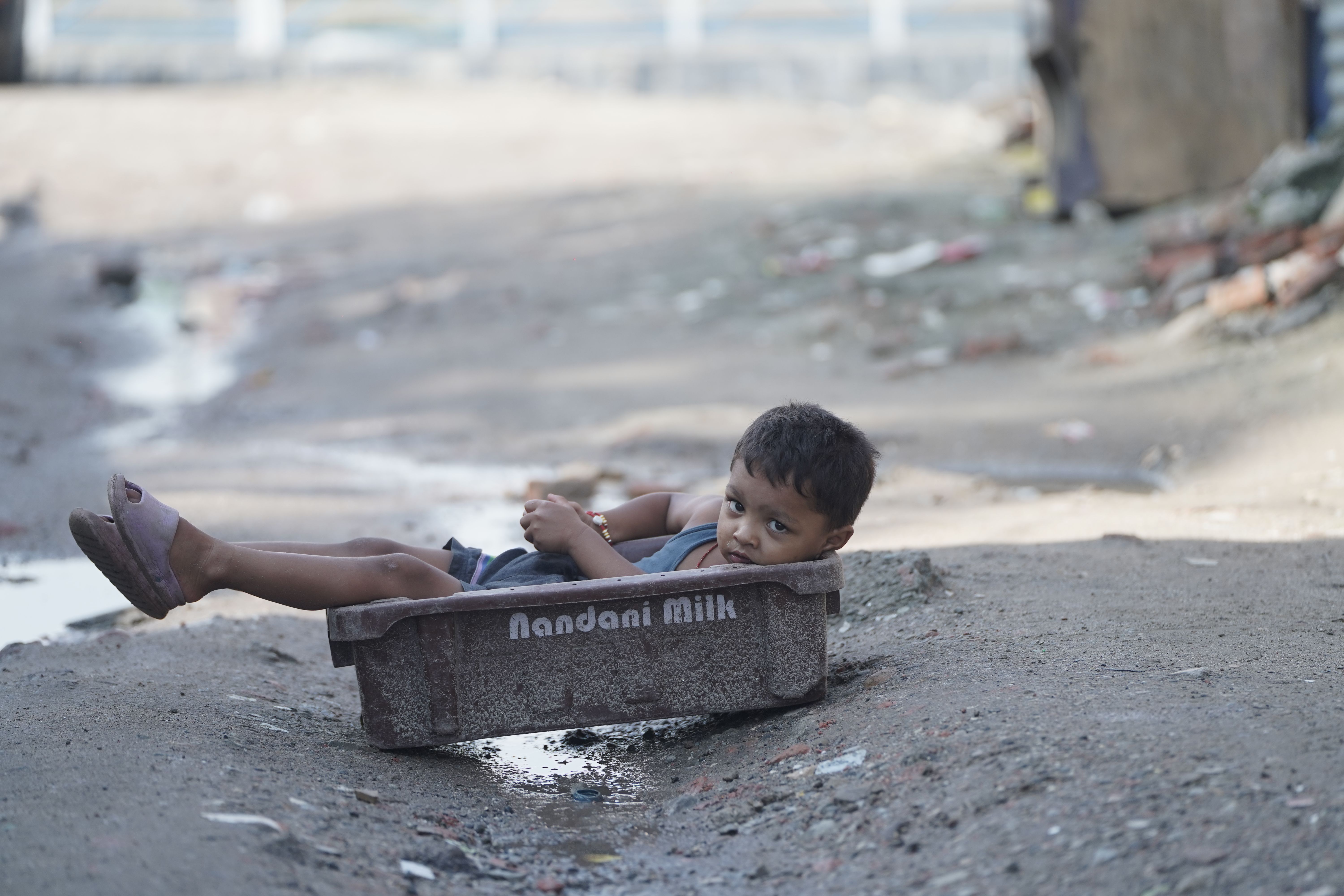 Young boy lounging in Nandani Milk crate on a dusty urban street, reflecting childhood innocence.