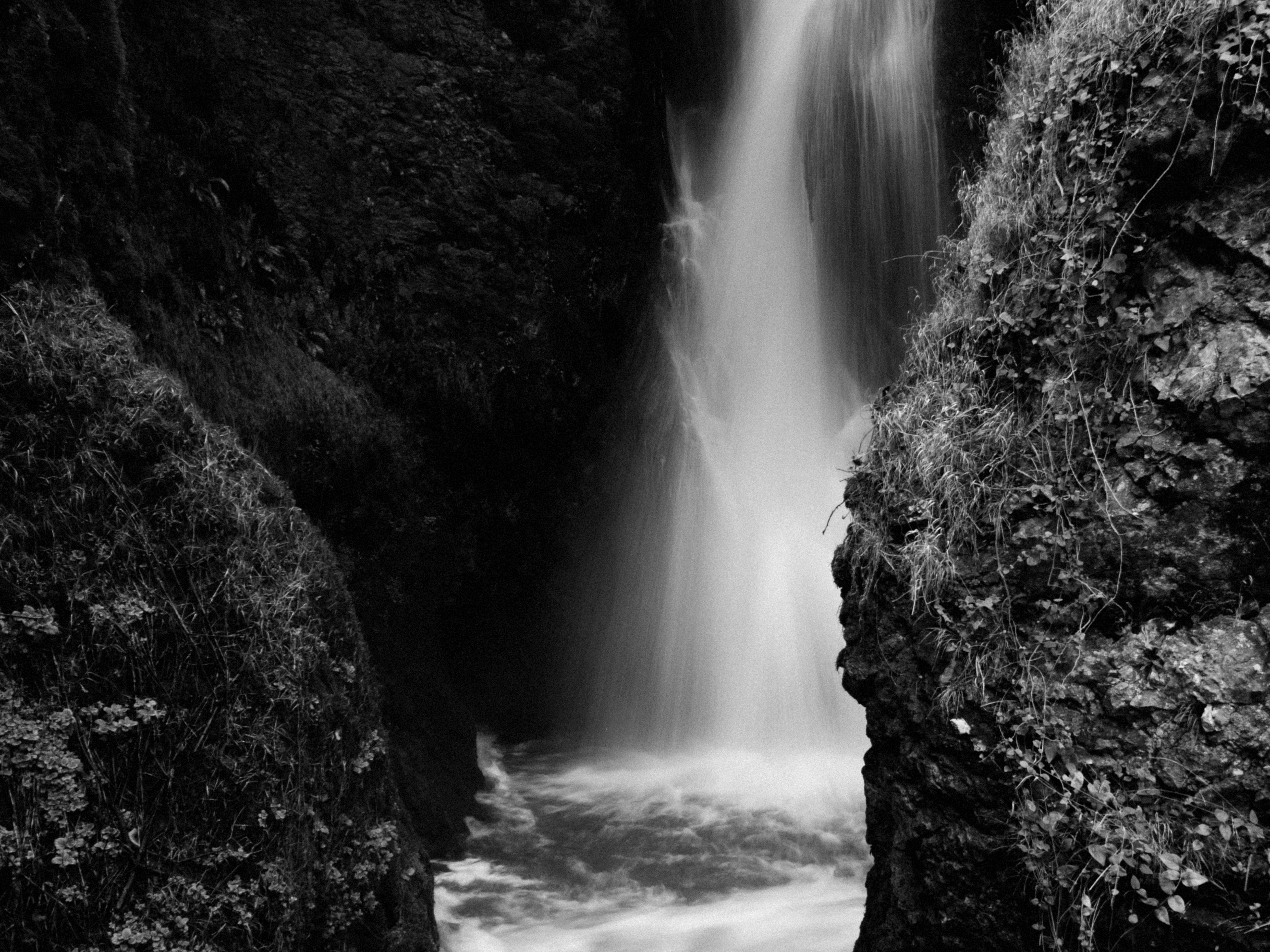 Ücretsiz Kayalık uçurumların arasına gizlenmiş, siyah beyaz karelerle yakalanmış, huzur dolu bir şelale. Stok Fotoğraflar