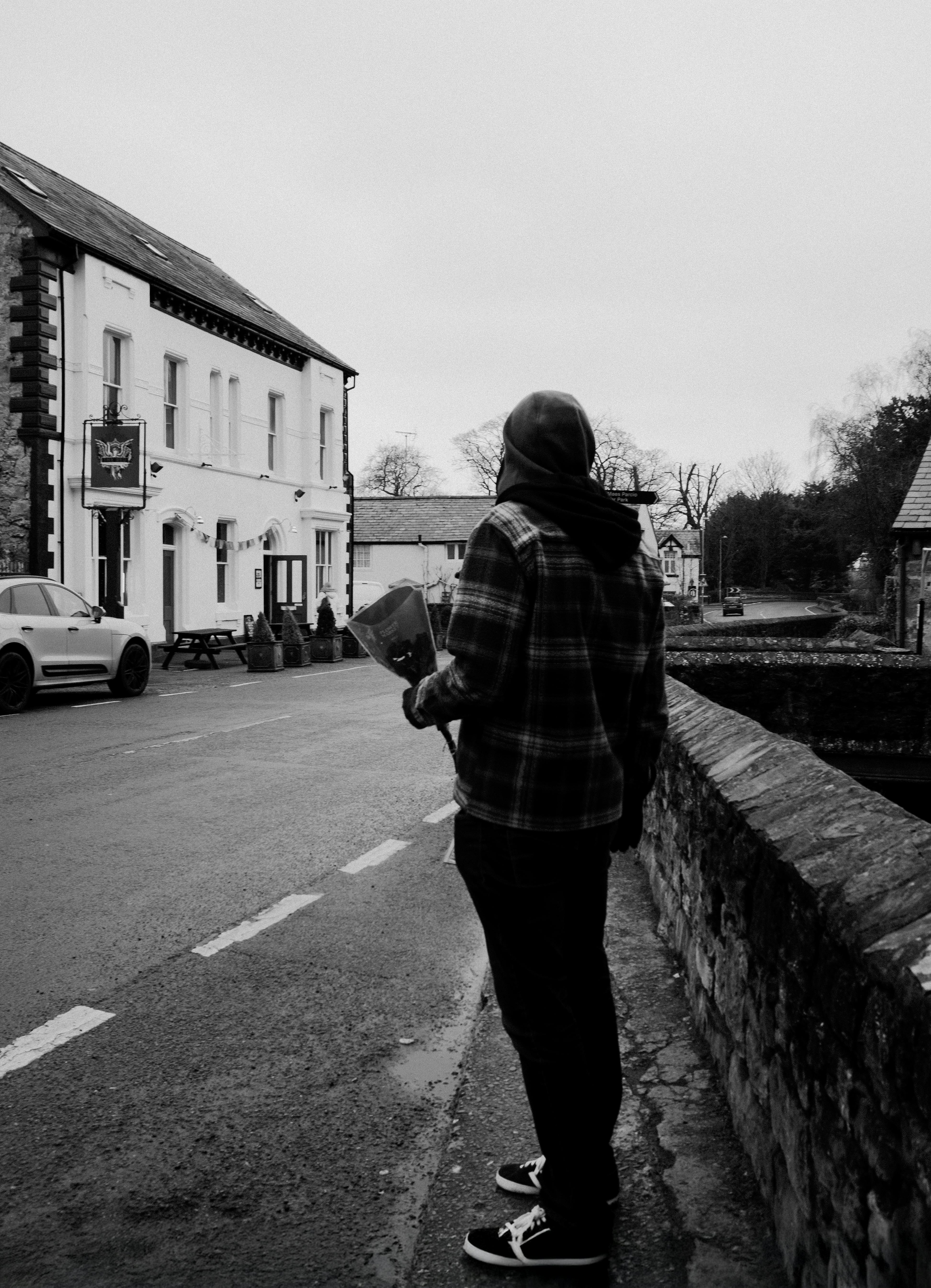 A person in a hoodie stands by a country road in a quaint town.