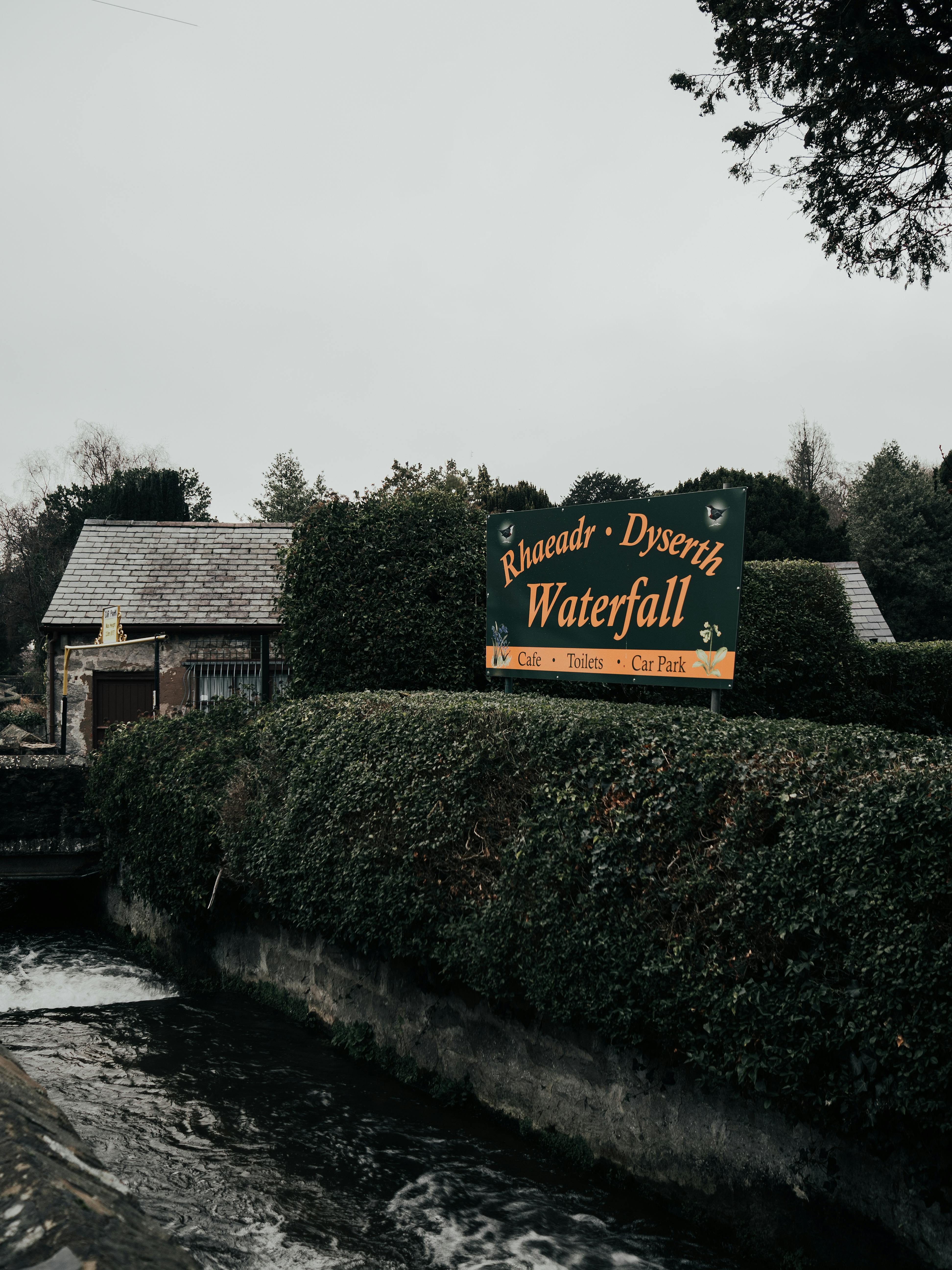 View of Rhaeadr Dyserth Waterfall sign with lush greenery in Dyserth, Wales.