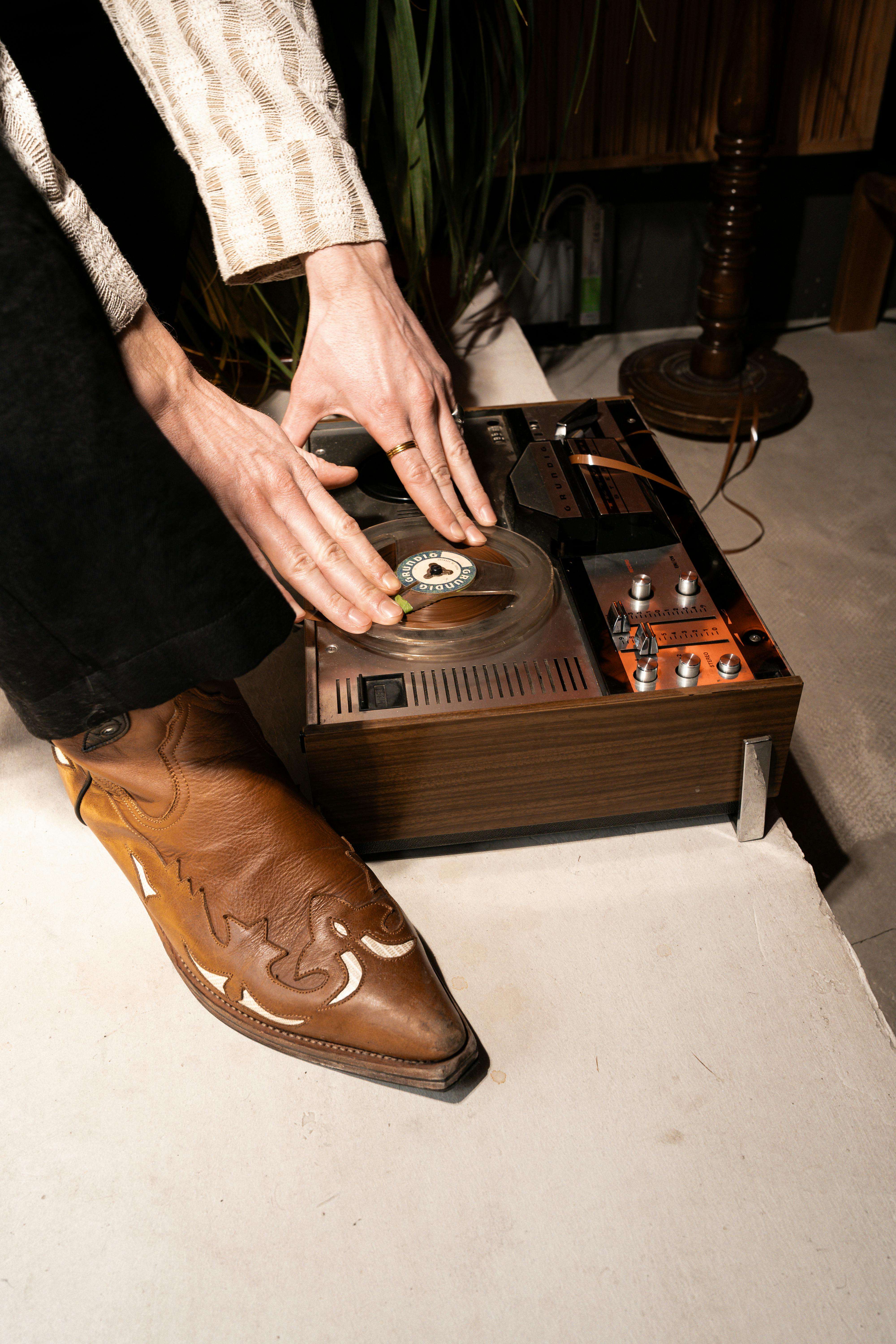 grátis Uma pessoa interage com um toca-discos antigo, destacando uma bota de cowboy. Ambiente interno. Foto profissional