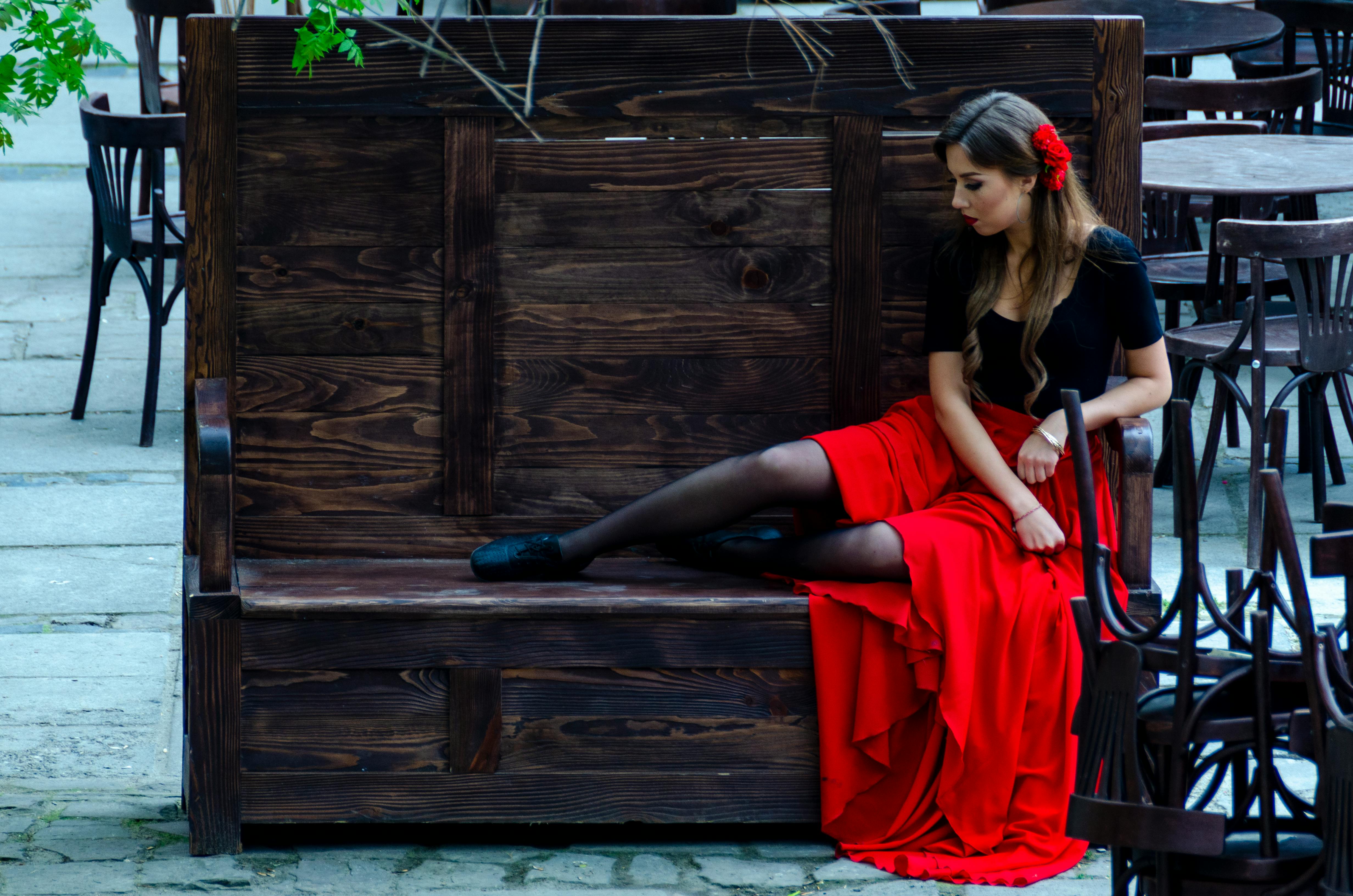 Gratis Ung kvinne i fasjonabelt rødt antrekk sitter på en rustikk trebenk utendørs. Arkivbilde