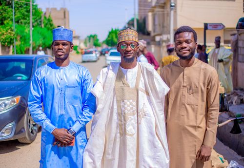 Free Three men pose together outdoors in traditional Nigerian attire, with a vibrant street background. Stock Photo