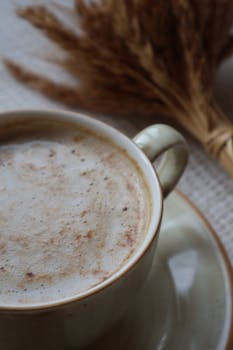 Warm foamy coffee in a cup with autumn wheat decor creates a cozy, inviting atmosphere.