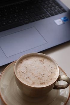 A warm cup of coffee sits beside a laptop in a cozy home office setting, perfect for productivity.