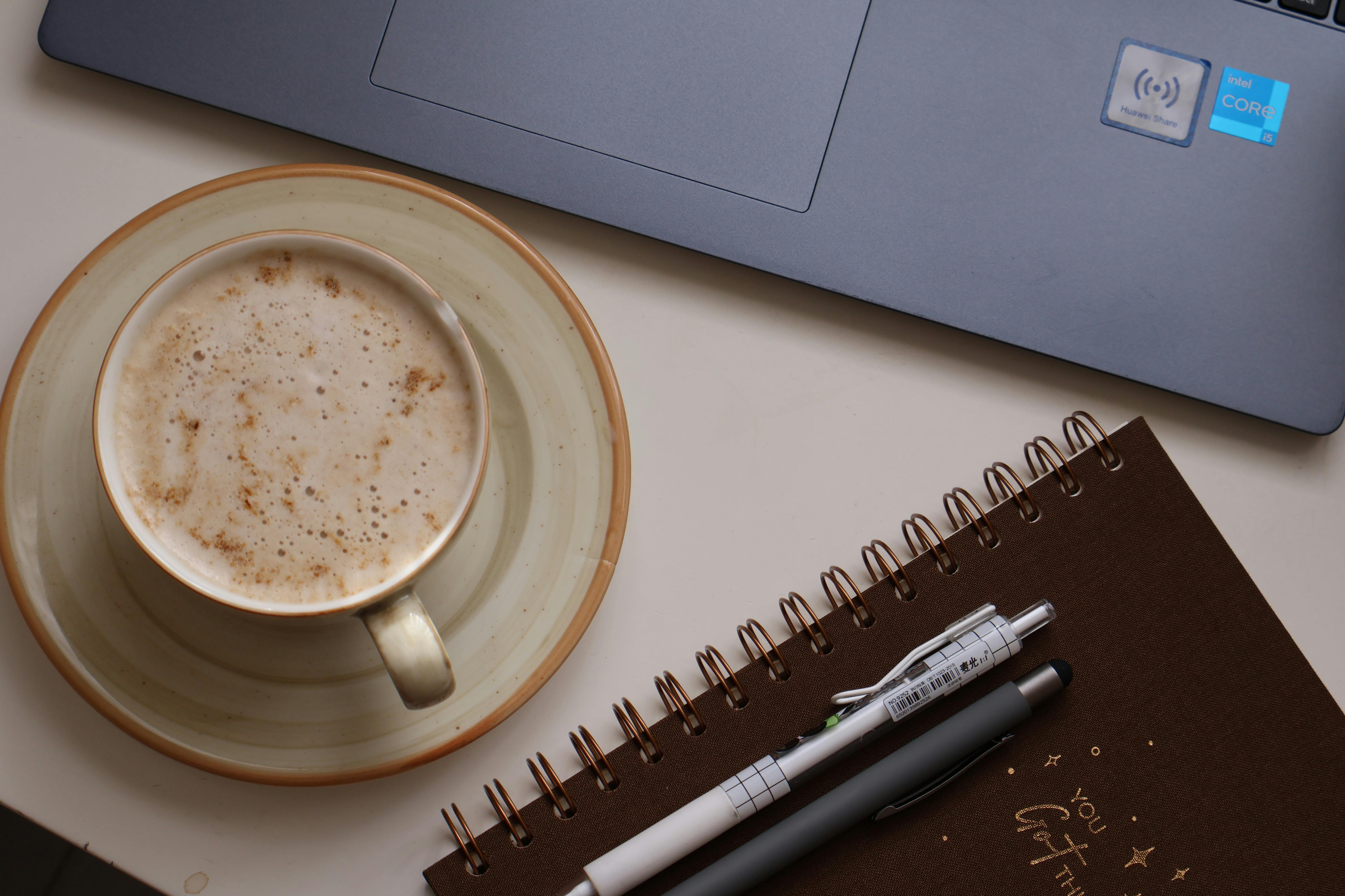 Warm indoor workspace featuring a laptop, coffee cup, and notebook with pens.