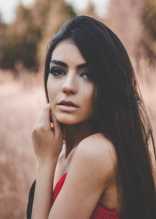 Free Portrait of calm young ethnic female with makeup and long dark hair touching face and looking at camera while standing in rural field Stock Photo
