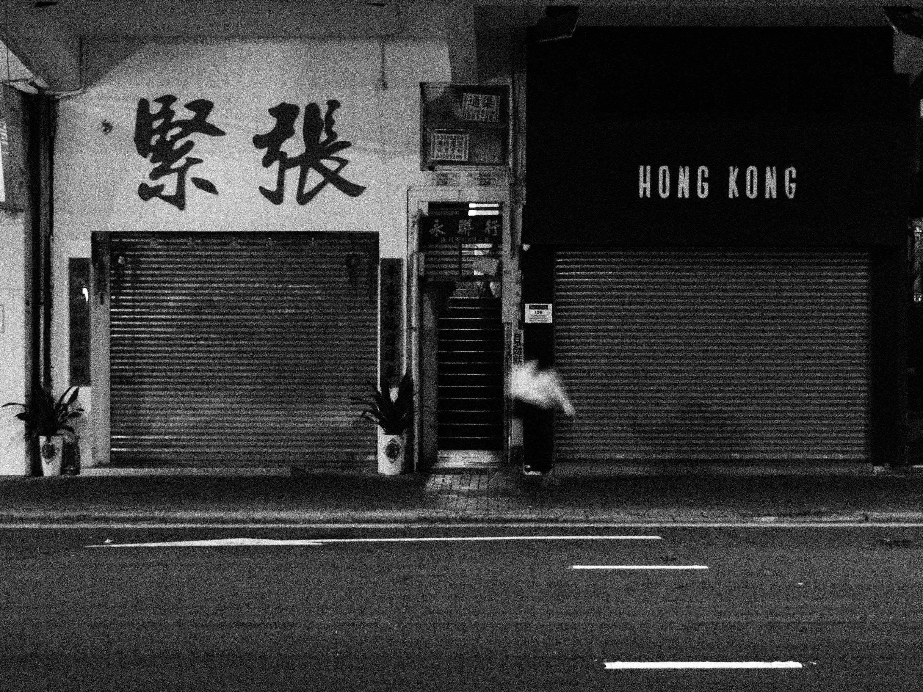 Moody black and white photo capturing a quiet Hong Kong street with closed shopfronts.