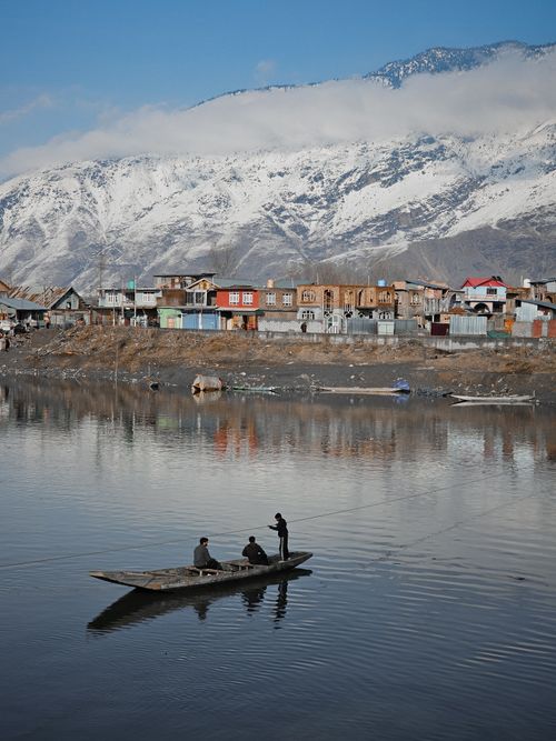 Free A picturesque boat ride on a tranquil mountain lake with snowy peaks and rustic homes. Stock Photo