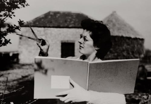 Woman in White Long Sleeve Shirt Holding a Book While Measuring A Leaf