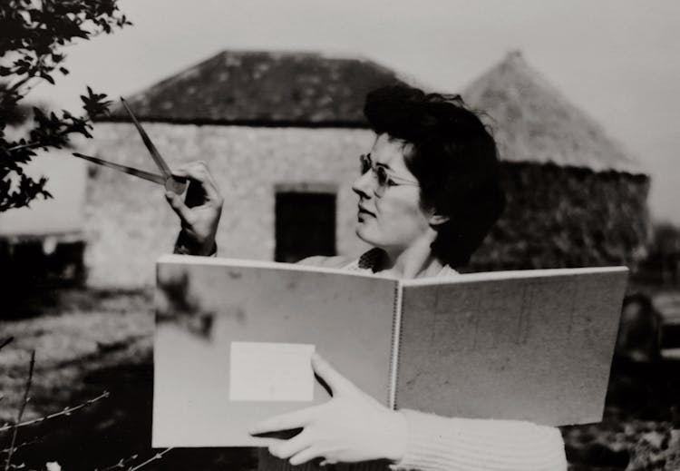 Woman In White Long Sleeve Shirt Holding A Book While Measuring A Leaf