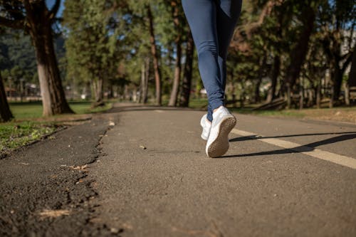 Person in Blue Denim Jeans and White Sneakers Walking on Road