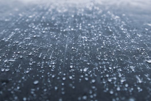 Close-up view of water droplets scattered on a dark textured surface, creating an abstract pattern.