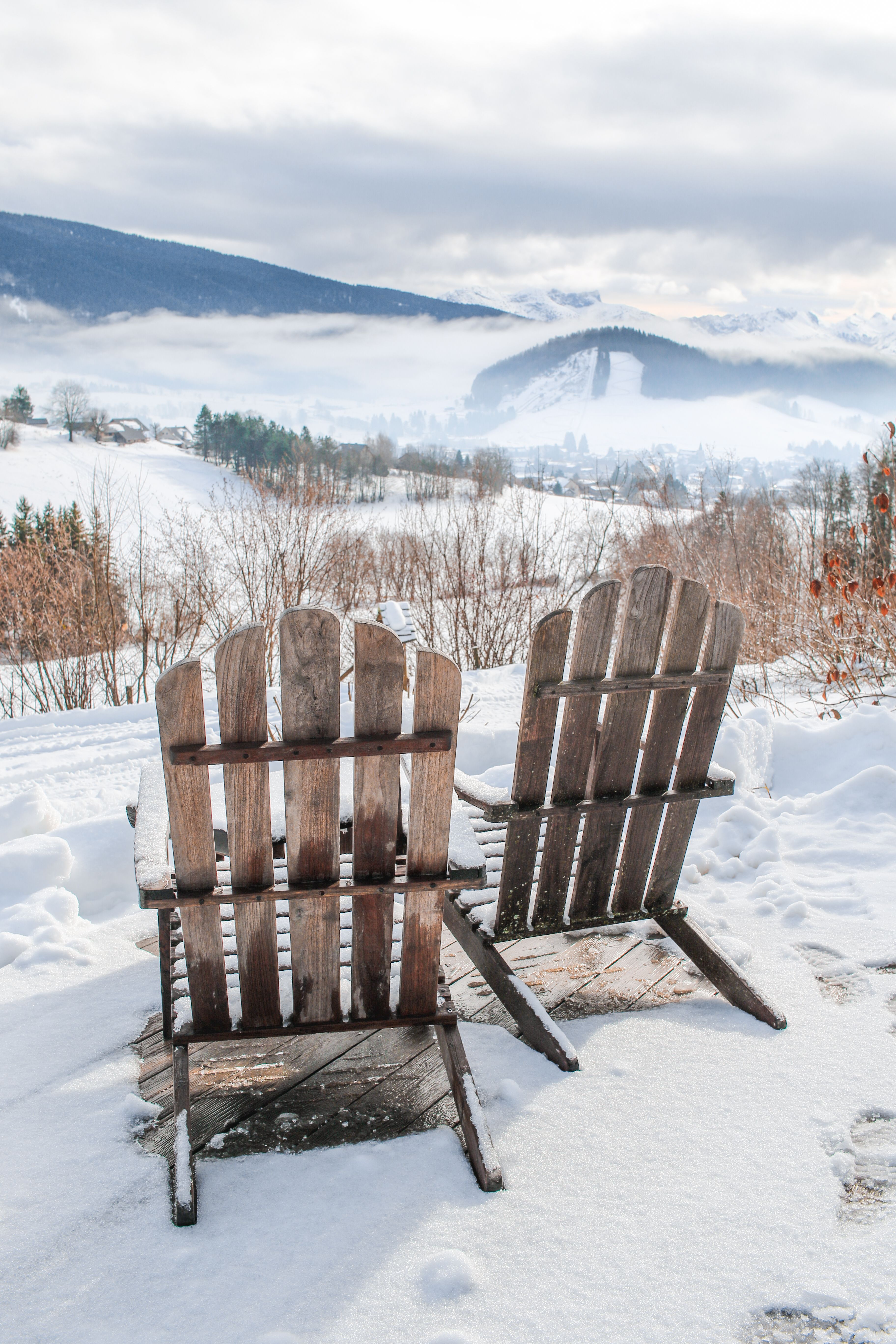 Wooden chairs on snow overlooking misty Vercors Mountains in France.