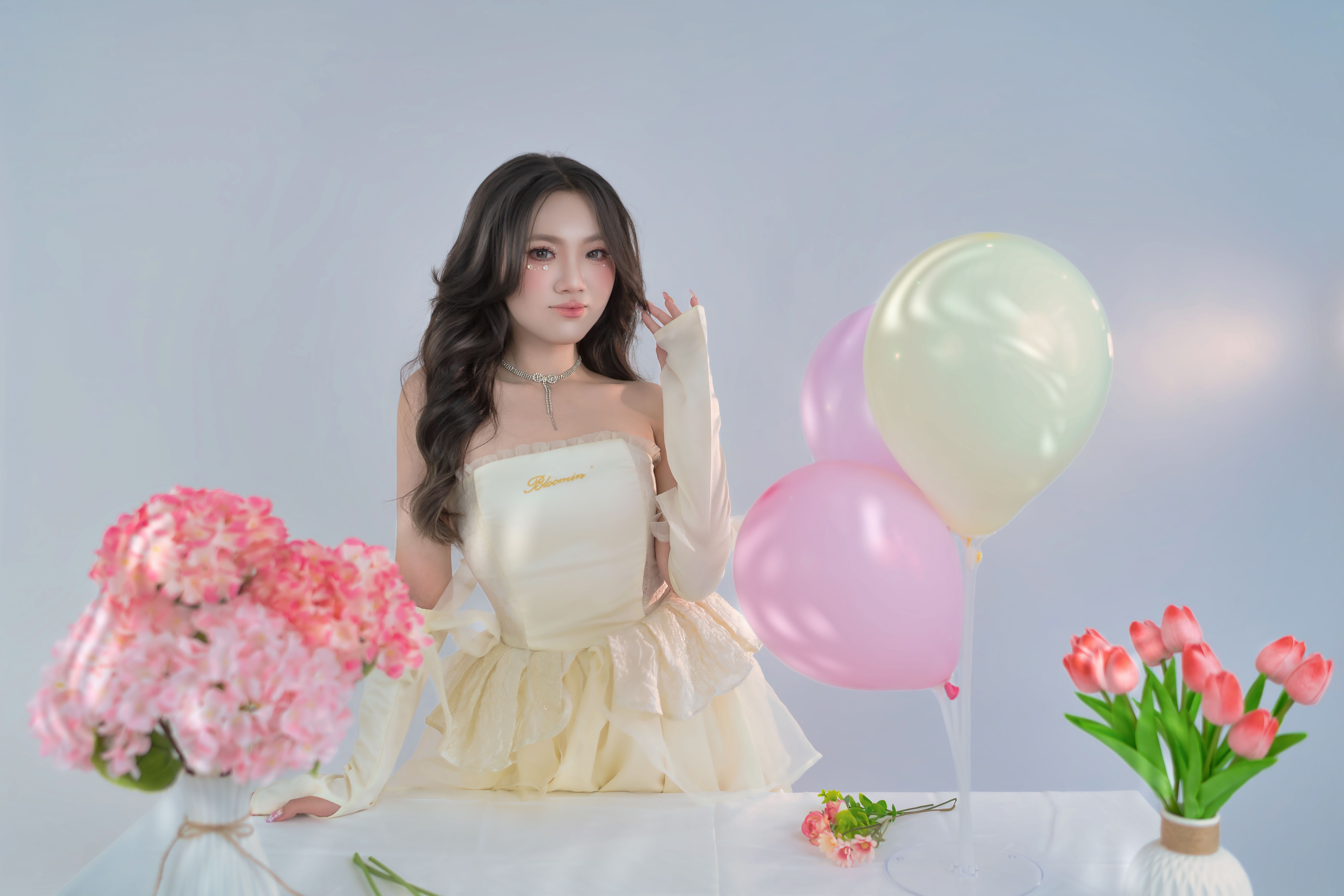 Elegant woman in a stylish dress with balloons and flowers, in a bright indoor setting.