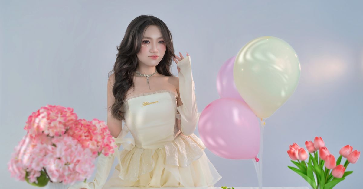 NewJeans posts surprise four-member video for fourth debut anniversary Elegant woman in a stylish dress with balloons and flowers, in a bright indoor setting.