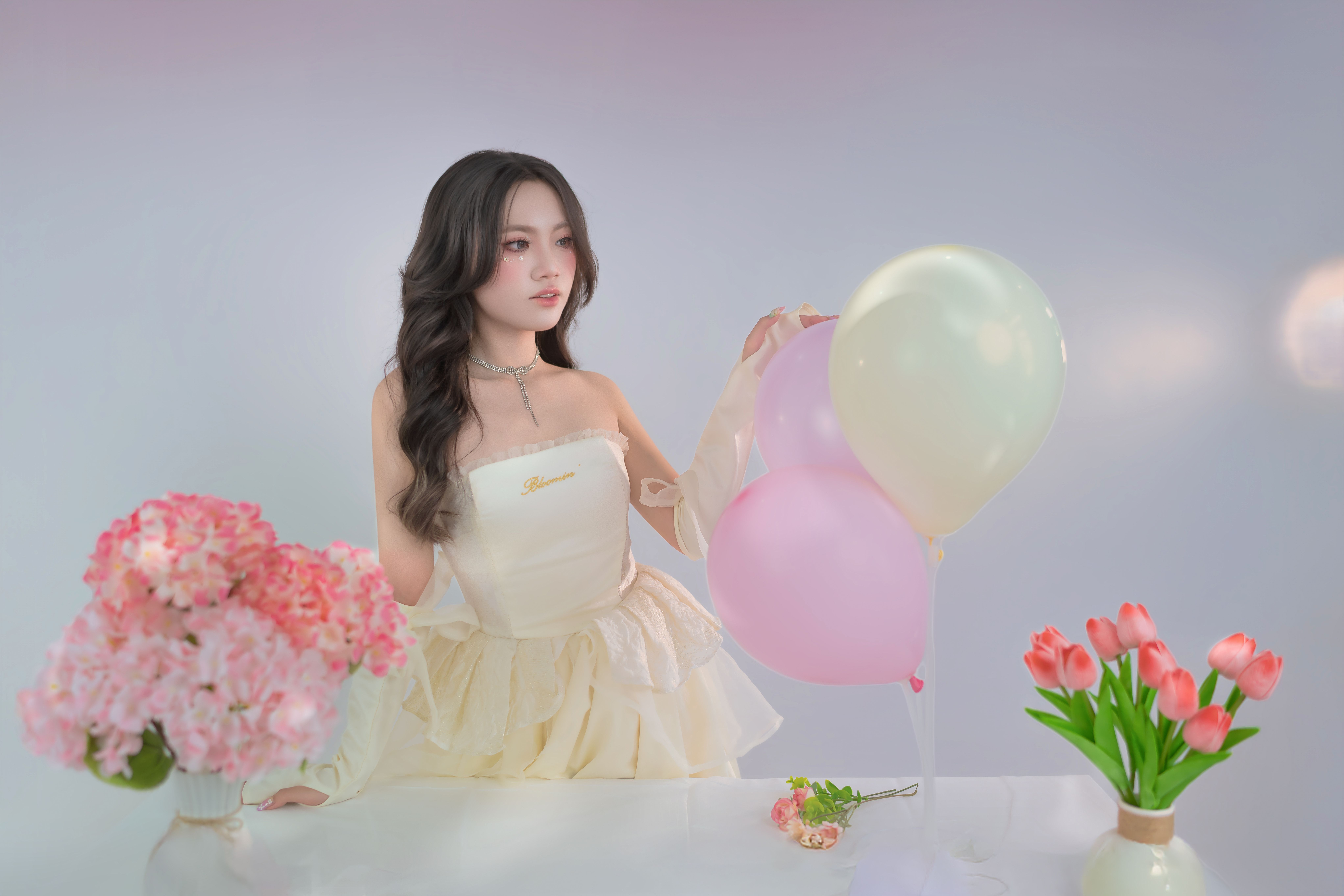 A woman in a stylish dress poses with pastel balloons and floral arrangements.
