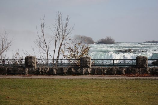 Serene view of Niagara Falls from a park, showcasing autumn foliage and tranquil waters.