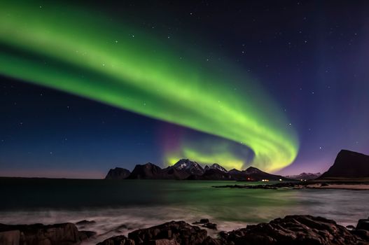 Stunning aurora borealis lights up the night sky above the snowy mountains and ocean.