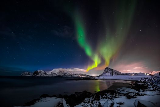 Stunning aurora borealis illuminating the night sky above snowy mountains and icy waters.