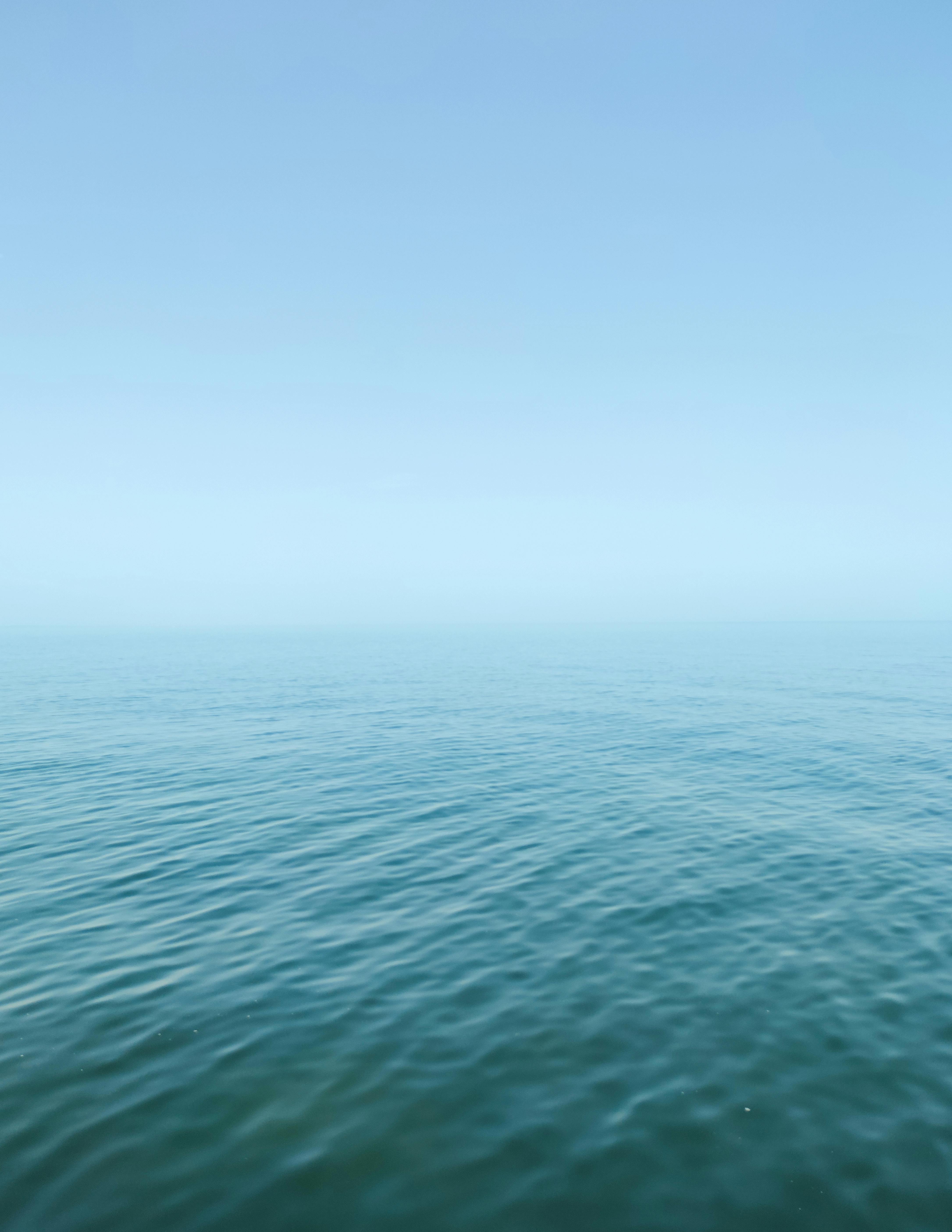 grátis Vista tranquila do oceano com ondas suaves sob um céu azul límpido, exalando serenidade e paz. Foto profissional